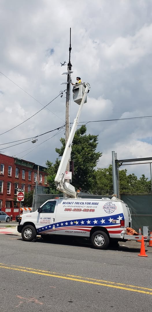 Bucket raised to a light pole at a street corner beside a brick building, with safety cones