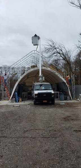 Bucket raised above the arched metal frame of a fabric-covered building under construction