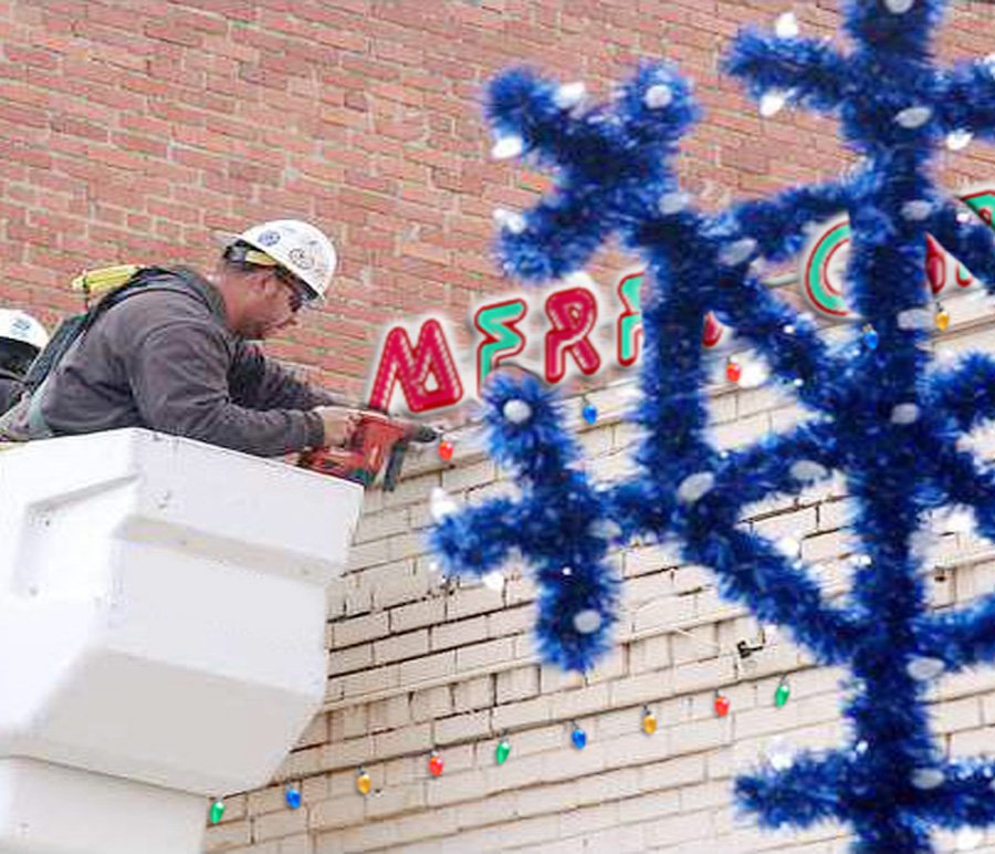 A worker in the bucket installing holiday lights and decorations along a brick building