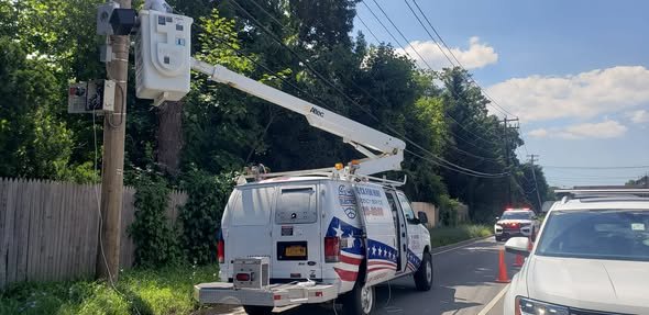 Bucket raised to equipment mounted on a wooden pole along a road, with cones behind the van