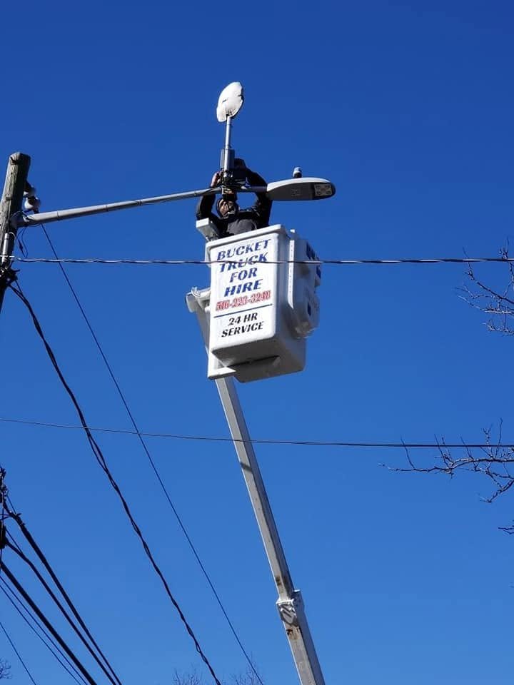 Our bucket, lettered Bucket Truck for Hire, 24 hour service, raised to the top of a street light against a blue sky