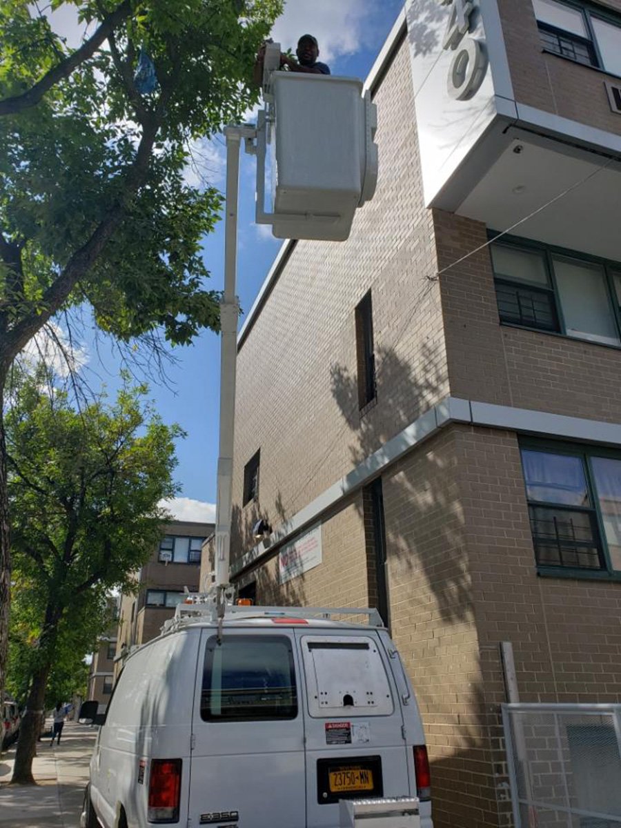 Our white bucket truck parked at the curb with the bucket raised to the third floor of a brick apartment building